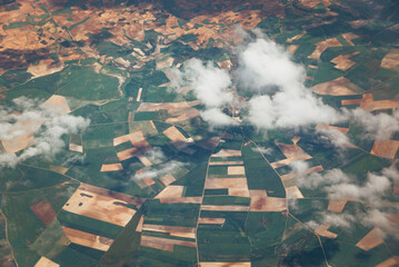 Patchwork landscape with white clouds covering a little village. Aerial view from fertile land...