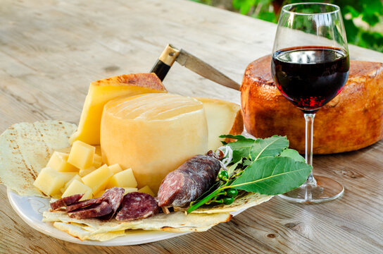 Vassoio con pecorino sardo e salsiccia secca di maiale, accompagnati da un calice di vino cannonau rosso, gastronomia sarda, cibo italiano 