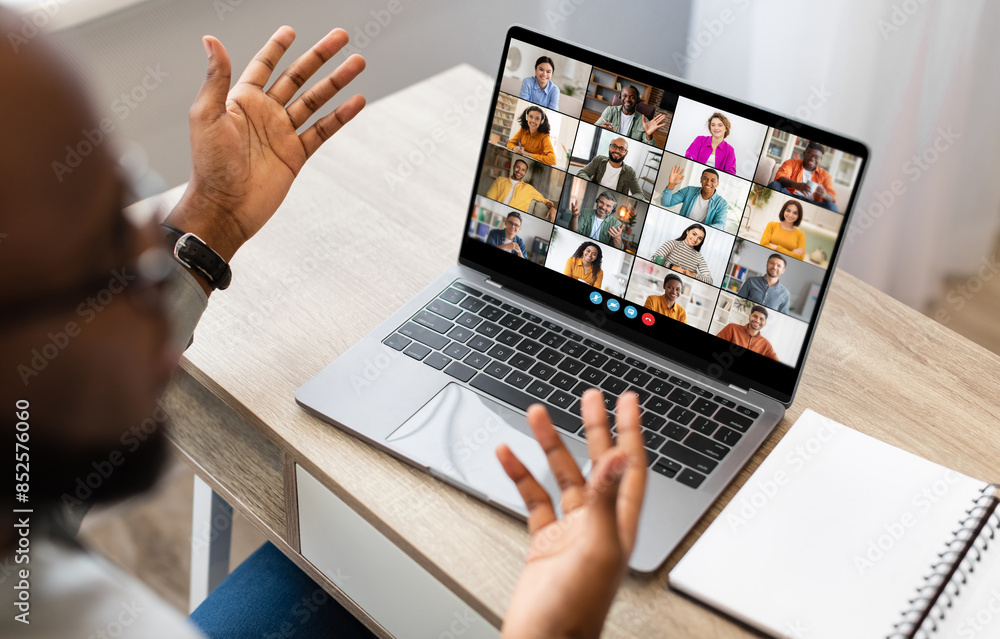Poster black man sits at a desk in front of a laptop screen, participating in a video conference meeting. h