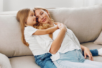 Mother and daughter sharing a joyful moment on a cozy couch against a clean, white background