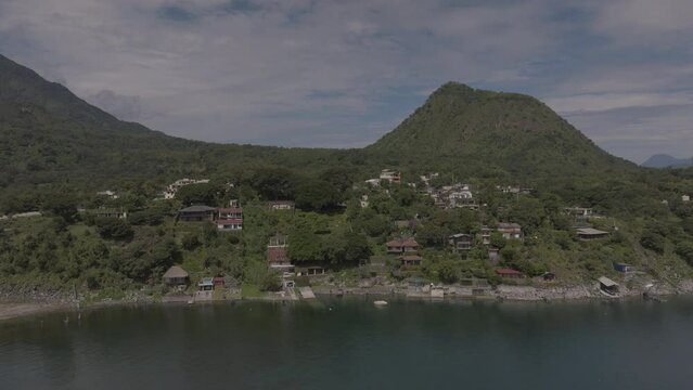 wide aerial capture of lake houses with mountains and lush greenery in background in lake atitlan guatemala