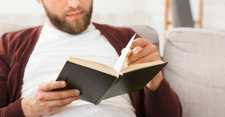 A man is seated on a couch, engrossed in reading a book. The man appears focused and relaxed,...