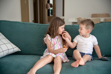 happy smiling children sitting together on the sofa, eating a croissant