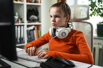A young student girl in a comfortable home office deftly types text on the keyboard.