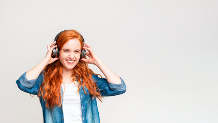 A woman with vibrant red hair is engrossed in listening to music through headphones. She appears...
