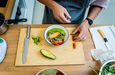 Chef at the kitchen preparing healthy quinoa bowl with avocado