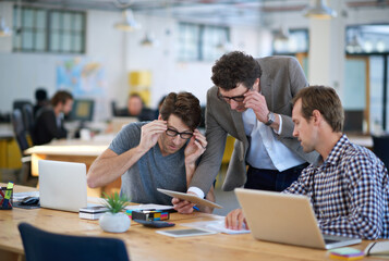 Fototapeta premium Businessmen, tablet and talking for teamwork, communication and creative planning together at office. Thinking, colleagues and tech for company startup, brainstorming or collaboration in workplace
