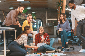 Diverse group of individuals sitting on the floor inside an office setting, engaged in a meeting or discussion.