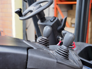 Close-up view of forklift controls showcasing levers and steering wheel in a industrial setting.