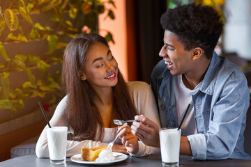 A young African American couple smiles warmly at each other while sharing a dessert and milkshakes...