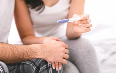 A woman shows a pregnancy test to her partner in bed, with a positive result indicated. The couple...