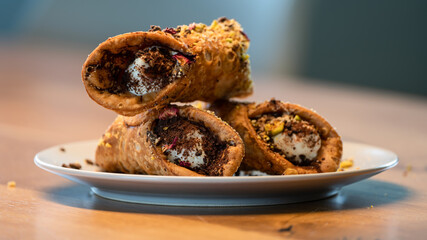 Three canolli, filled with mascarpone cheese, with pistachios sprinkles on a plate