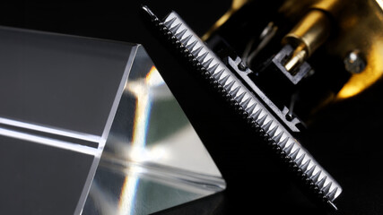 Sharp blade of a professional shaving trimmer next to a glass prism on a dark background. Gadget...
