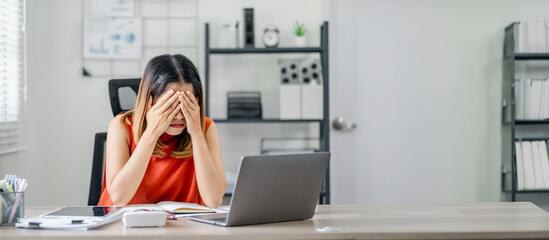 A woman is sitting at a desk with a laptop and a computer mouse. She is looking at the screen with...