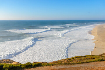 Fototapeta premium Aerial view of sandy beach and Atlantic ocean with big waves in Nazare, Portugal. Surfing paradise town in Portugal, Europe