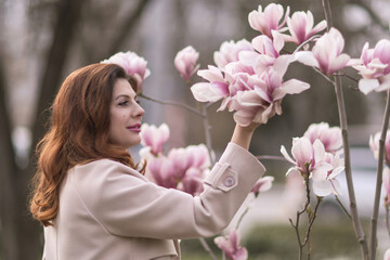 Fototapeta premium Woman magnolia flowers, surrounded by blossoming trees., hair down, wearing a light coat. Captured during spring, showcasing natural beauty and seasonal change.