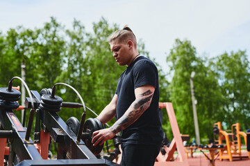 Caucasian male athlete training with fitness equipment, outdoor workout in a summer park