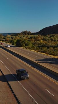 Two-ways roads going through the humpy mountainous territory. Transport moving by the highways at the backdrop of blue skies. Vertical video
