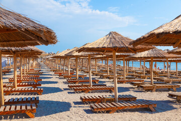 Sunshades with thatched roof and sun loungers on the beach by the sea.