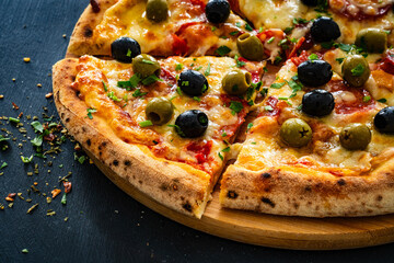 Circle pizza chorizo with black and green olives and mozzarella on wooden table
