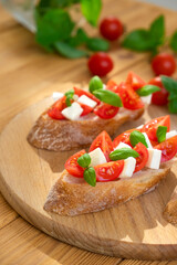 Caprese bruschetta with tomatoes, mozzarella cheese and basil in sun rays on wooden board. Traditional Italian appetizer, snack or antipasto. Vegetarian food. Healthy eating. Mediterranean food.