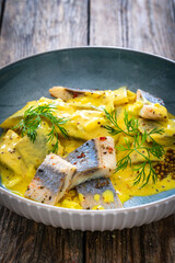 Marinated herring fillets in mustard sauce with dill and lettuce on wooden table
