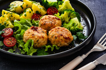 Cooked meatballs, boiled broccoli, boiled potatoes and fresh vegetables on wooden table
