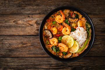 Tom Yam Kung soup - Thai soup with shrimps and rice noodles served in black bowl with chopsticks on wooden table
