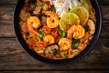 Tom Yam Kung soup - Thai soup with shrimps and rice noodles served in black bowl with chopsticks on wooden table
