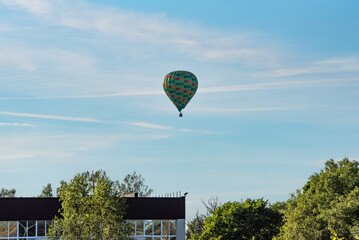 a flying hot air balloon over the roof of a building over the treetops