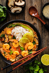 Tom Yam Kung soup - Thai soup with shrimps and rice noodles served in black bowl with chopsticks on wooden table
