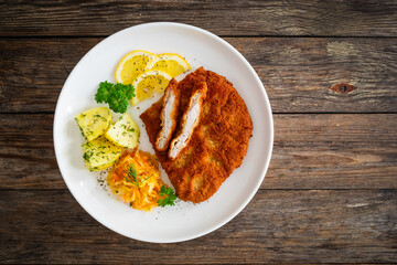 Crispy breaded fried pork chop, boiled potatoes and sauerkraut salad on wooden table
