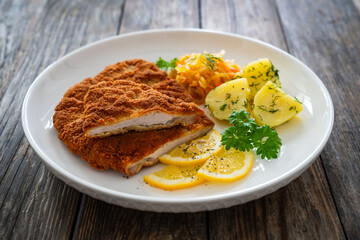 Crispy breaded fried pork chop, boiled potatoes and sauerkraut salad on wooden table
