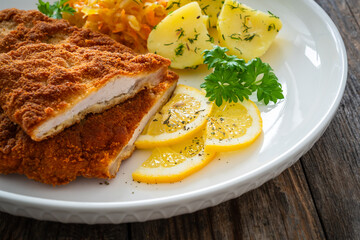 Crispy breaded fried pork chop, boiled potatoes and sauerkraut salad on wooden table
