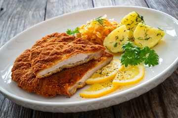 Crispy breaded fried pork chop, boiled potatoes and sauerkraut salad on wooden table

