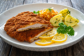Crispy breaded fried pork chop, boiled potatoes and sauerkraut salad on wooden table
