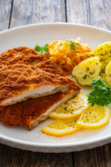 Crispy breaded fried pork chop, boiled potatoes and sauerkraut salad on wooden table
