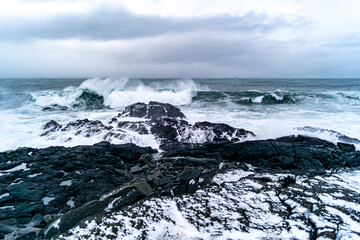 Cliffs in Valahnúkamöl in Iceland in winter time covered with snow, stormy sea, high waves and black rocks