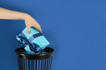 Hand throwing gift box into trash bin or waste bucket. Rejected bad gift concept