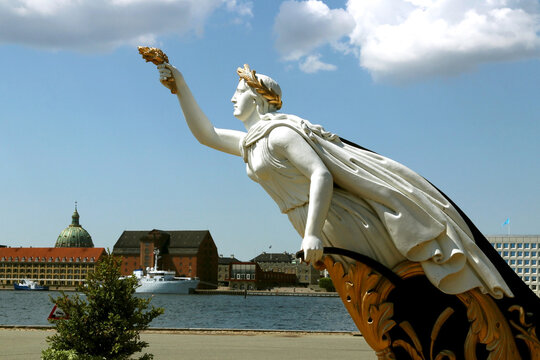 The figurehead is a woman holding gilded ears of wheat in her right hand and a plow in her left. Installed on the waterfront in Copenhagen, Denmark.