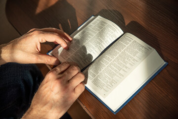 Fototapeta premium Hands of man holding Holy Bible at home. Lifestyle, natural aesthetic light.