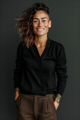 Woman with short shaved hair smiling in black shirt and brown pants.
