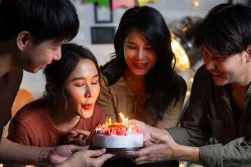 friend birthday cake. young asian woman blows out a birthday cake that friends brought for a birthday party. celebrating Birthday party. Group of friends smiling enjoying party