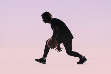 Silhouette of a young basketball player dribbling ball in studio with pink background