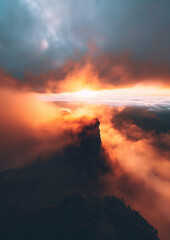 Naklejka premium Dramatic sunset over misty mountains, with clouds illuminated by the setting sun. Perfect for landscape and nature photography.