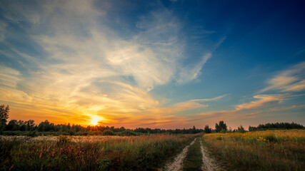 Rural road in a field against the backdrop of a summer sunset.