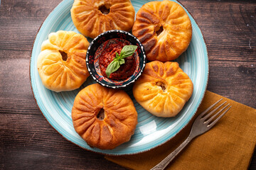 Tatar national dish Belyashi or open pies with meat and tomato sauce on a blue plate on a wooden background.