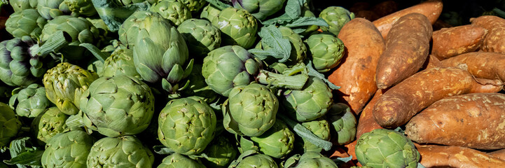 Obraz premium Fresh artichokes and sweet potatoes on display at a farmers market, ideal for healthy eating and vegetarian recipes, related to Thanksgiving and harvest festivals