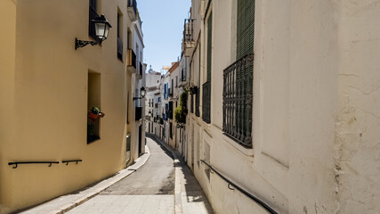 Quaint sunlit European alley with traditional white architecture and cobblestone paving, related to travel, culture, and summer holidays in Mediterranean regions