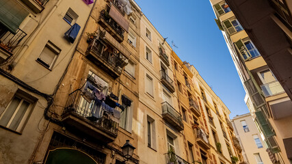 Urban laundry day concept showing clothes hanging from balconies in a narrow European street under a clear blue sky, depicting everyday city life